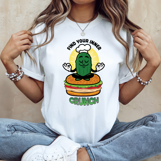 Person wearing a white t-shirt with a graphic design of a pickle on a burger, with text 'Find your inner crunch'.