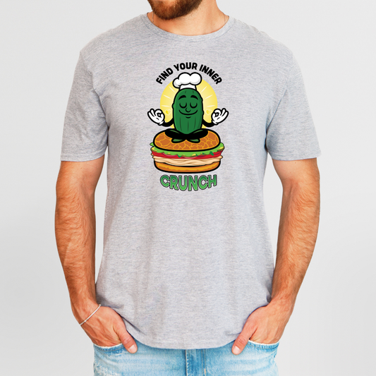 Person wearing a gray t-shirt with a cartoon pickle chef and burger graphic on a light gray background