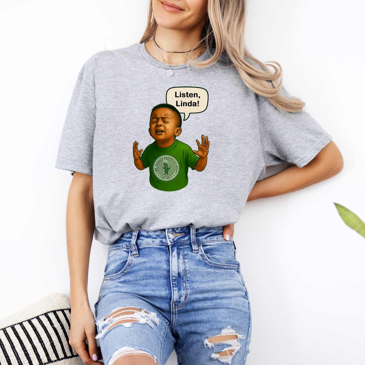 Person wearing a gray t-shirt with a graphic of a child and text, standing against a white background.