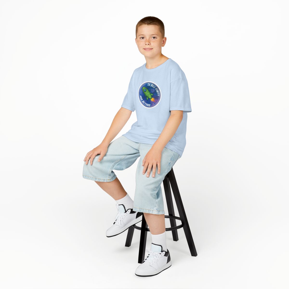 Young boy sitting on a stool wearing a light blue t-shirt with a colorful logo and light blue jeans.