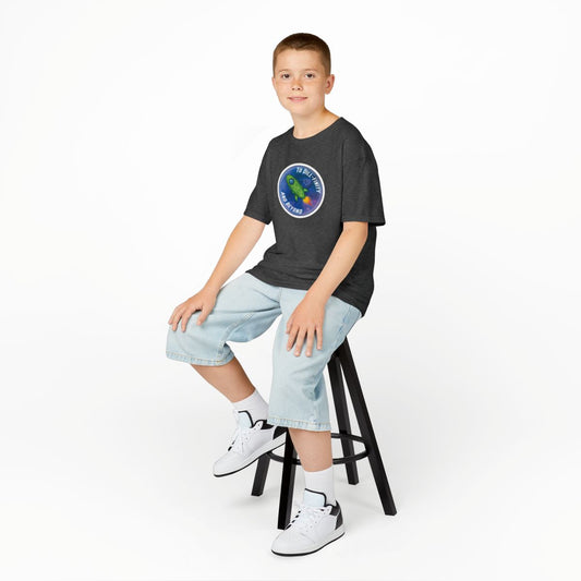 Young boy sitting on a stool wearing a dark t-shirt with a colorful logo, light blue jeans, and white sneakers.